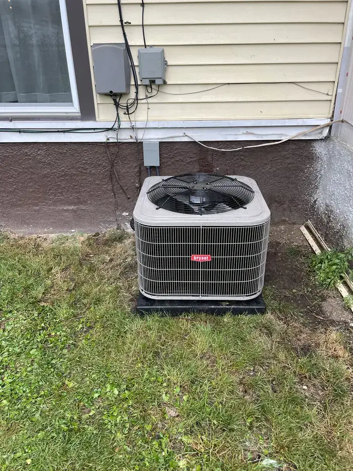 A replacement Bryant condenser on a pad beside a home with pale siding